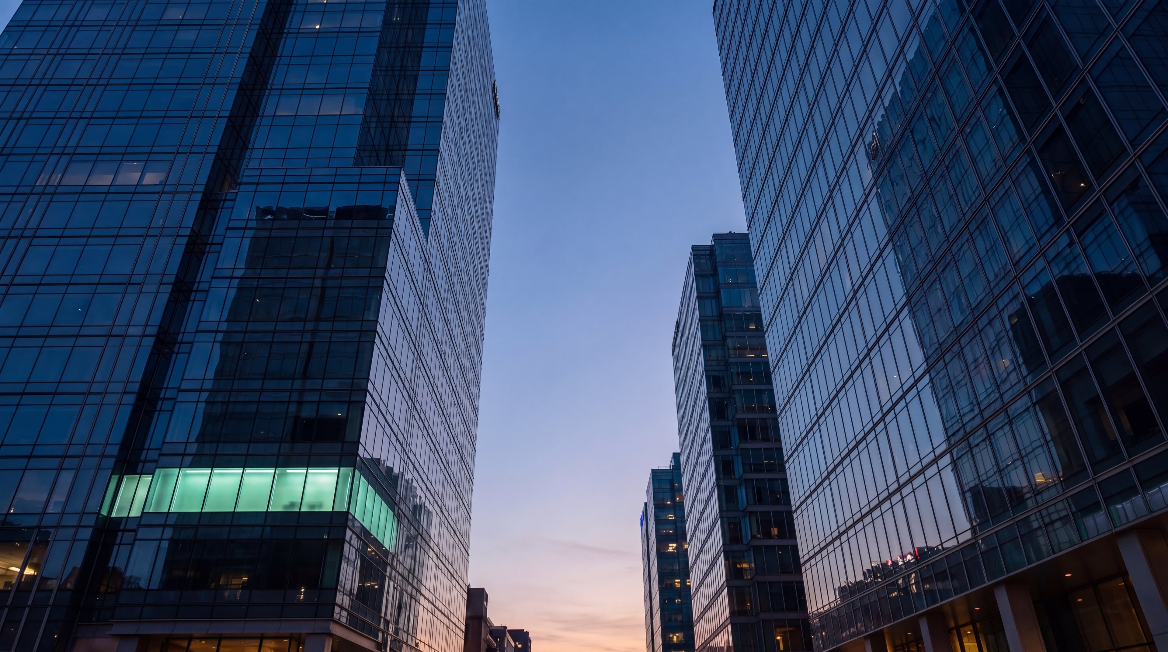 Torres de oficinas a la hora azul con el atardecer al fondo de la calle, un piso todavía encendido en verde menta