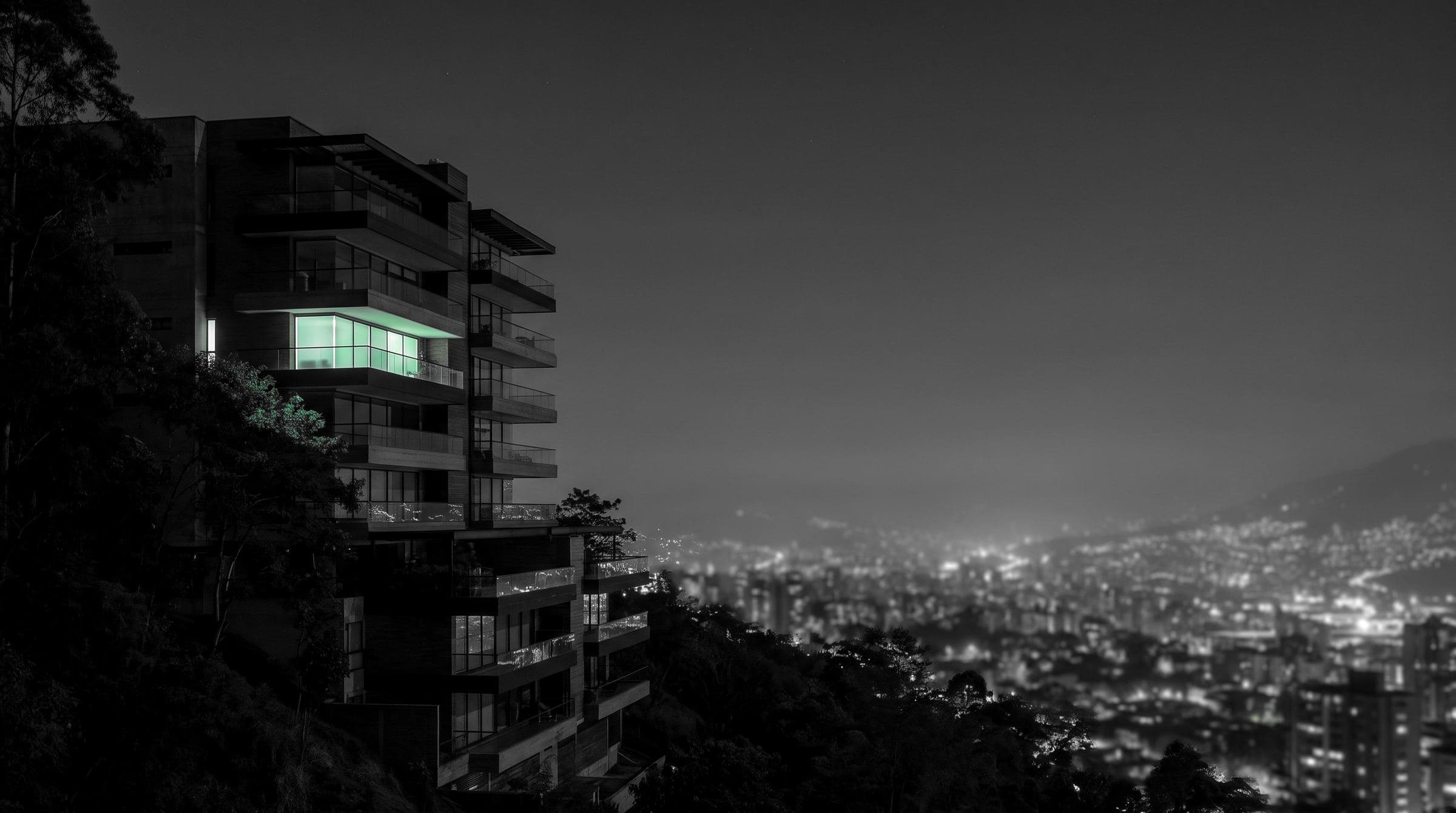 Un edificio de apartamentos sobre Medellín de noche en blanco y negro, una ventana encendida en verde menta