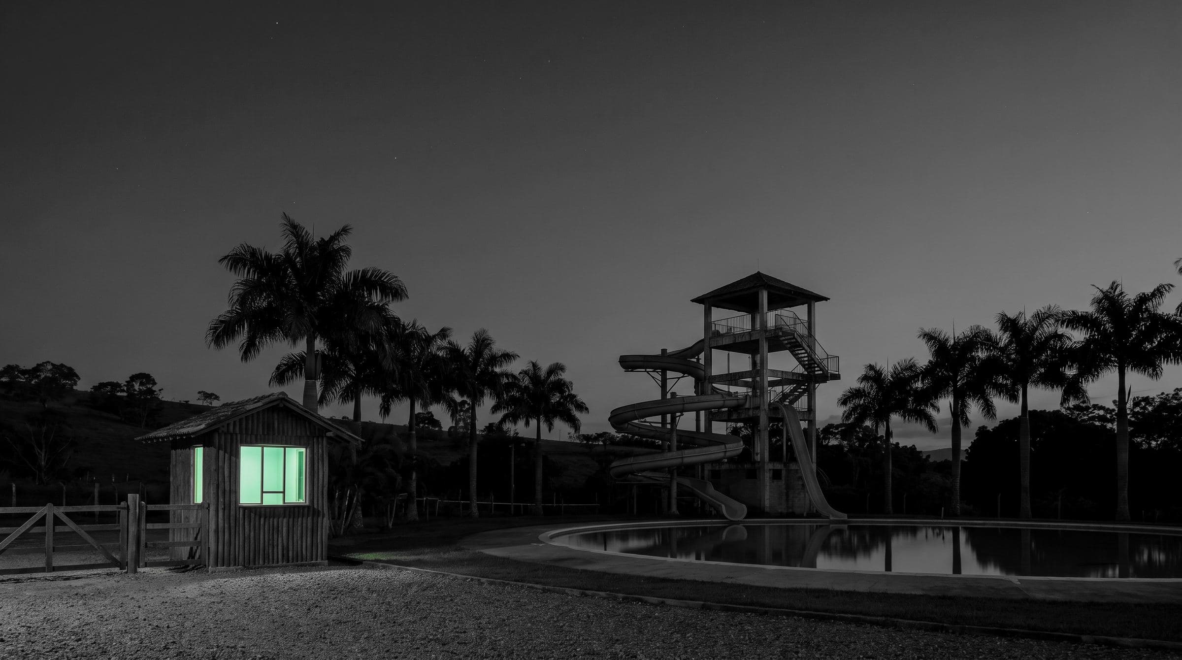 Un parque temático de noche en blanco y negro, la taquilla encendida en verde menta