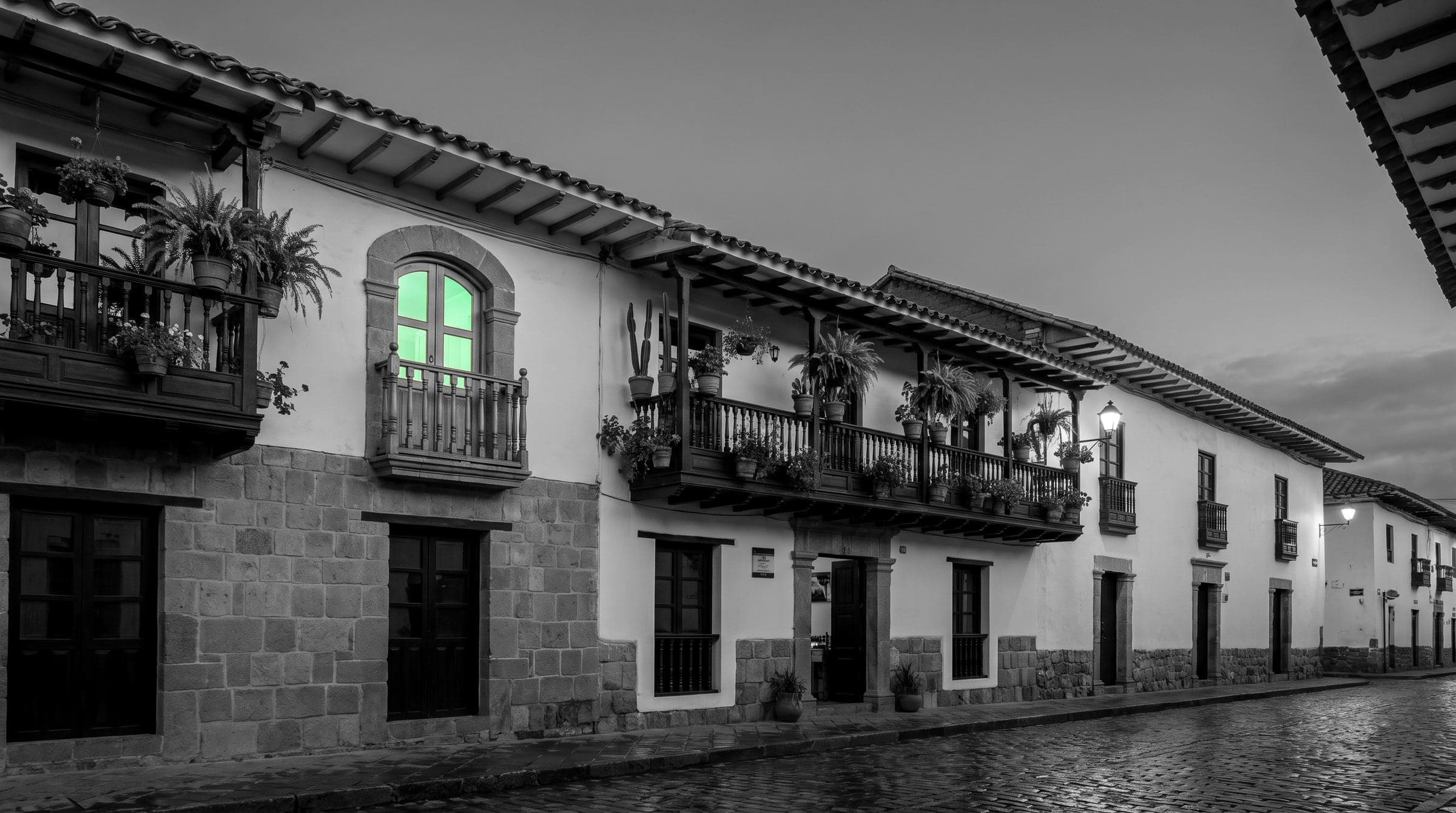 Una calle colonial con un hostal al atardecer en blanco y negro, un balcón encendido en verde menta